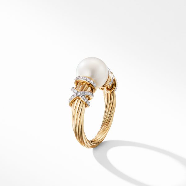 A gold ring with a twisted band design, adorned with a large white pearl at its center. The band is accented with small, sparkling diamonds arranged in a crossing pattern, adding an elegant touch to the luxurious piece of jewelry. The ring is set against a white background.