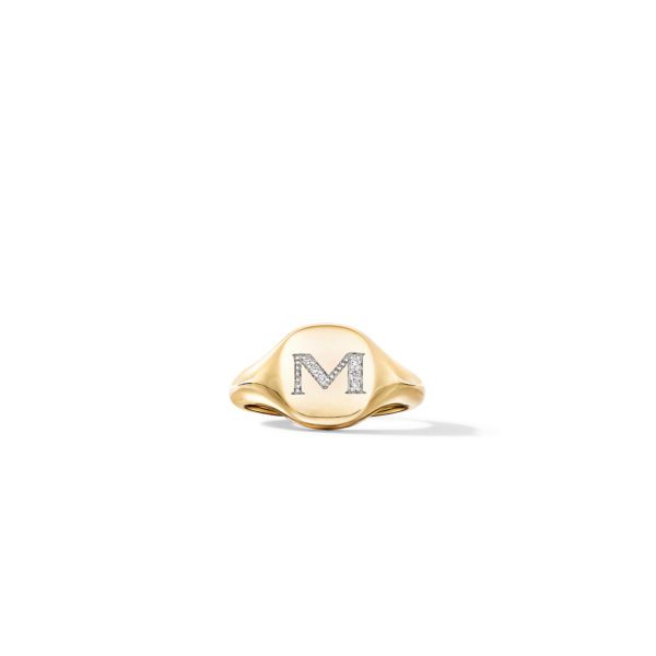 A gold signet ring with the letter "M" encrusted with small diamonds in the center. The ring sits on a plain white background, highlighting its elegant and polished design.