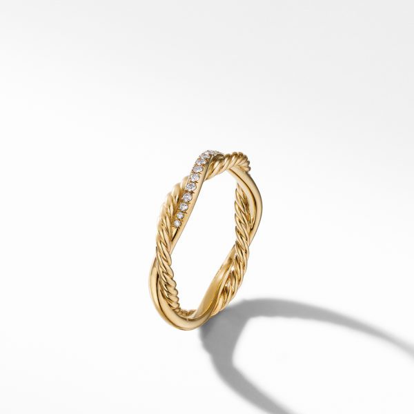 Minimalist gold ring with a twisted design, partially encrusted with small diamonds on one side, casting a shadow on a white background.