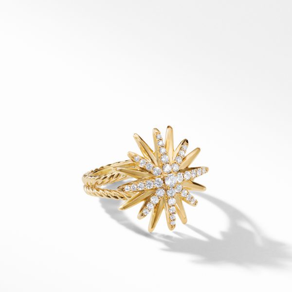 A gold ring with a starburst design featuring multiple pointed rays, each adorned with small diamonds. The band has a twisted rope pattern, and the ring casts a soft shadow on the white background.