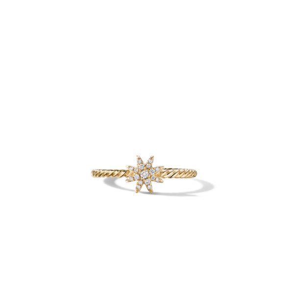 A gold ring with a twisted band features a starburst design at its center, encrusted with small sparkling diamonds. The ring is set against a plain white background.