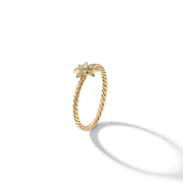 A gold ring with a twisted band design. The ring features a small, star-shaped cluster of diamonds at the top. The ring casts a soft shadow on a white background.