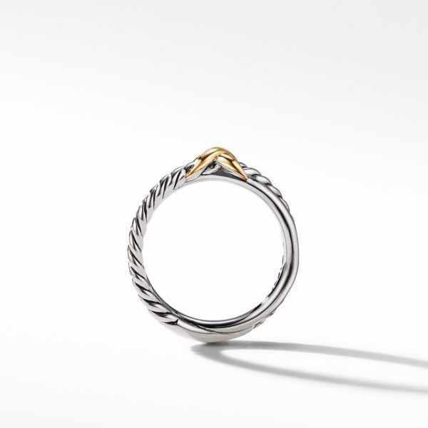 A close-up image of a silver ring with a twisted rope design and a small gold accent at the top center, set against a plain white background. The ring's shadow is visible on the surface below.