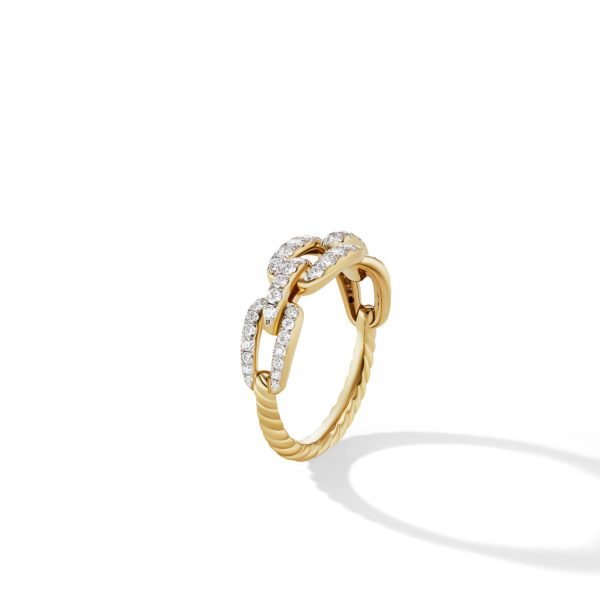 A close-up of a gold ring with a twisted band and three interconnected links at the top, partially encrusted with small, sparkling diamonds. The ring casts a soft shadow on a white background.