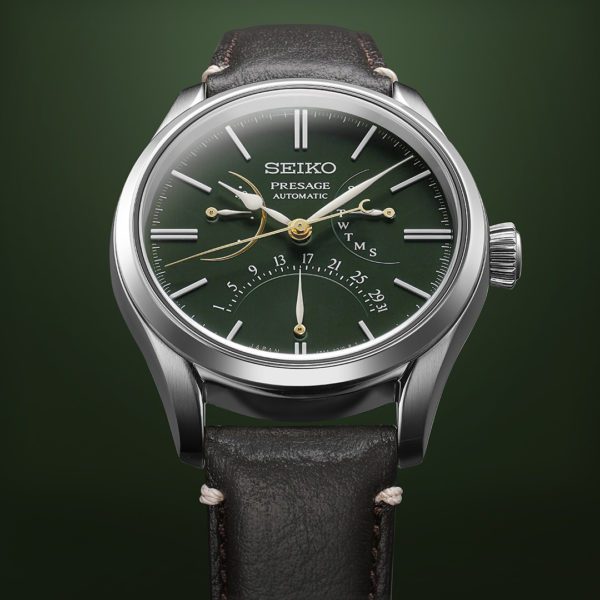 The Seiko SPB295 Presage - Craftsmanship Series Urushi Dial Limited Edition wristwatch boasts a deep green dial adorned with gold-toned hands and markers. This exquisite timepiece features week and date indicators, a silver case, and a black leather strap, all showcased against a stunning green gradient background.