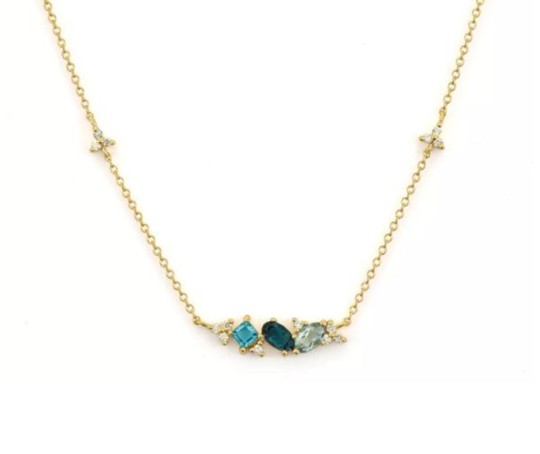 The Jude Frances Provence Princess Stone Necklace with Blue Topaz Elements is a gold chain necklace featuring four blue gemstones and small diamond accents arranged in a delicate design at the center. The stones vary in shape and shade, creating an elegant and symmetrical pattern, with multiple small diamonds also spaced along the chain.