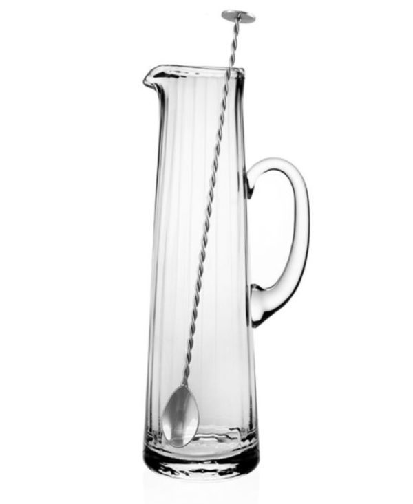 The William Yeoward Corinne Tall Cocktail Jug with Spoon is a clear glass pitcher featuring a handle on the right side, accompanied by a long, twisted metal stirring spoon that has a flat disc on one end and a spoon on the other. Both the pitcher and spoon are currently empty.