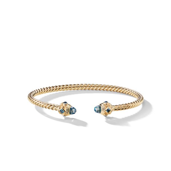 A gold twisted rope bangle bracelet with open ends, each adorned with a blue gemstone set in gold. The bracelet has a delicate and elegant design, casting a light shadow on a white background.