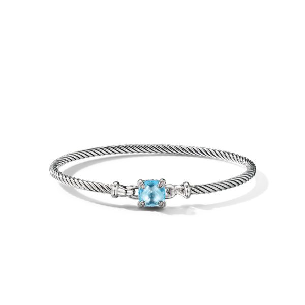 A thin, twisted silver bracelet with a light blue gemstone set in a square-shaped setting at its center. The gemstone is held by four prongs and flanked by small silver accents, adding elegance to the bracelet's minimalist design.