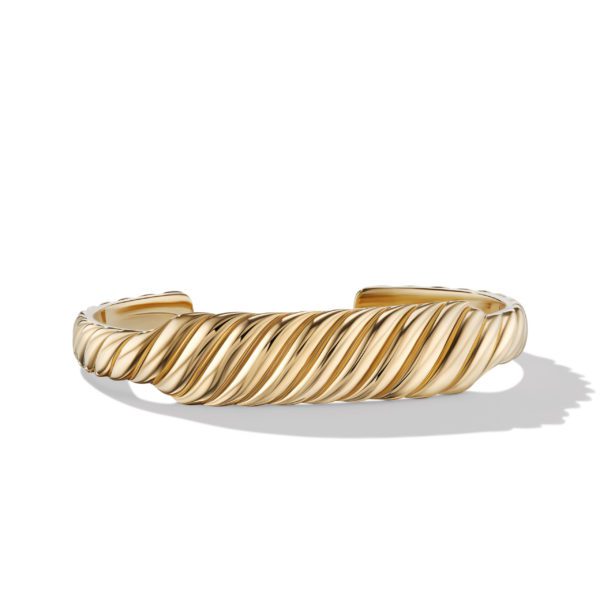 A gold cuff bracelet is displayed against a white background. The bracelet features a twisted rope design, creating a textured and elegant appearance. The shadows are cast on the surface, enhancing its three-dimensional look.