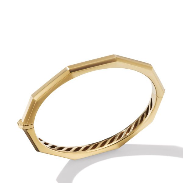 A gold bangle bracelet with a geometric, octagonal shape and sleek, polished finish is pictured against a white background. The bracelet features a subtle clasp mechanism for opening and closing.