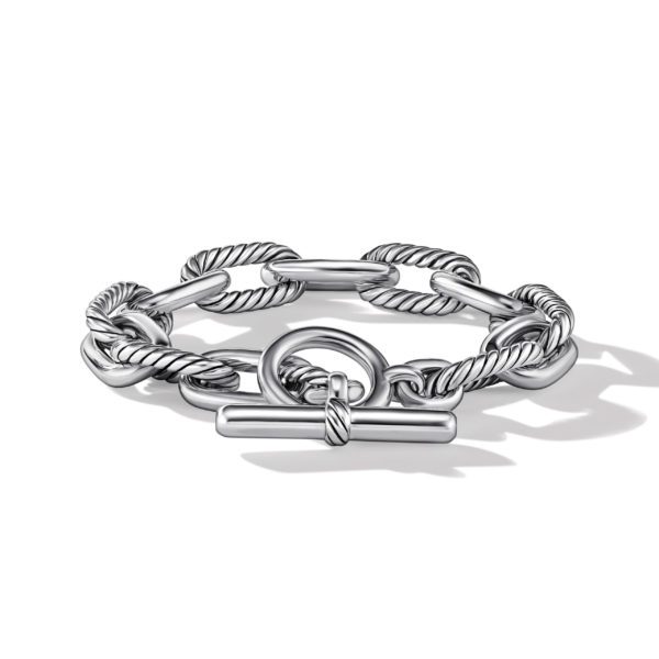 A silver bracelet featuring intertwined rope-like links and a T-bar clasp closure is showcased on a plain white background. The bracelet casts a soft shadow underneath, highlighting its intricate design and polished finish.