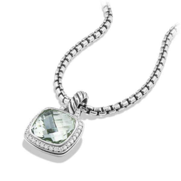 A silver necklace featuring a box chain and a pendant with a cushioned square green gemstone, surrounded by small clear stones. The pendant has a textured bail connecting it to the chain, set against a white background.