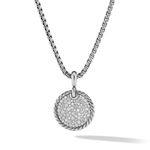 A silver necklace with a round pendant featuring intricate detailing and embedded small gemstones. The pendant hangs from a chunky chain with a box-like pattern. The overall design is elegant and sophisticated, reflecting light beautifully.