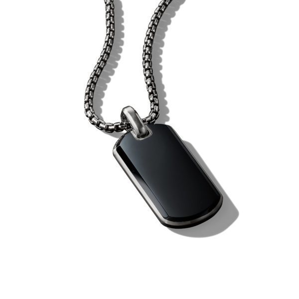 A dog tag-shaped black pendant hangs on a sleek silver chain with box links, set against a white background. The pendant has a glossy finish, and the chain casts a small shadow.