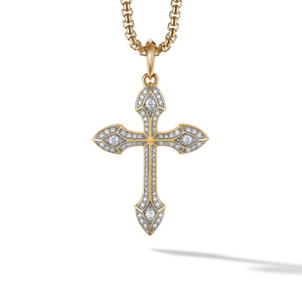 A gold cross pendant with intricate detailing and adorned with numerous small diamonds hangs from a gold chain. The chain is also finely crafted with a series of interlinked circular shapes. The pendant casts a soft shadow on the white background.