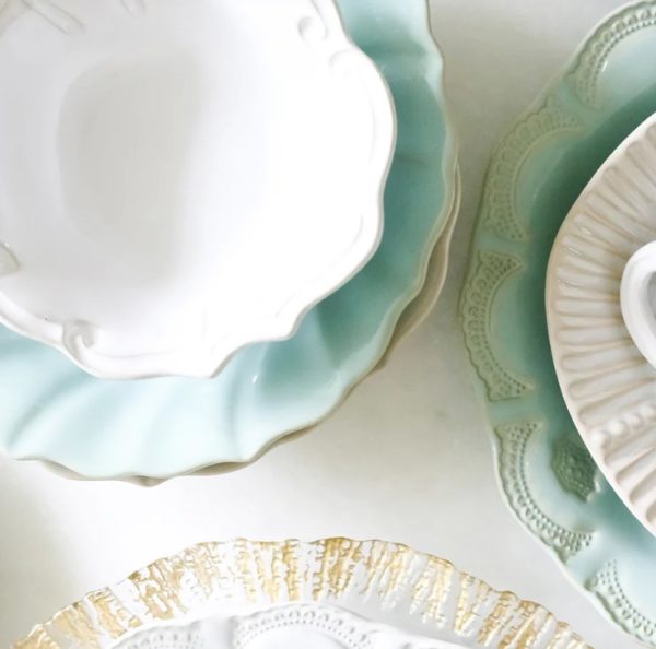 A photo displaying the Vietri Incanto Ruffle Salad Plates in pastel shades of green, blue, and white. The plates feature intricate designs and embossed patterns, arranged closely together on a light-colored surface.