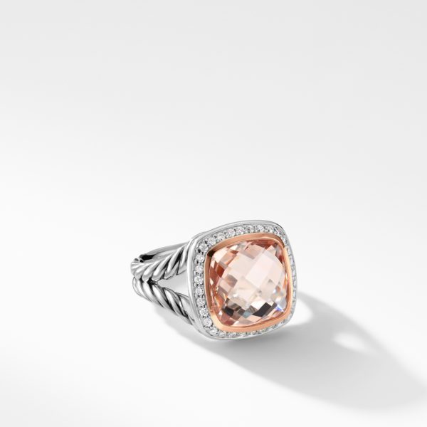 A silver ring with a twisted band features a large, square, faceted peach-colored gemstone set in the center. The gemstone is surrounded by small, sparkling clear stones, creating an elegant and sophisticated appearance. The ring is displayed on a white background.