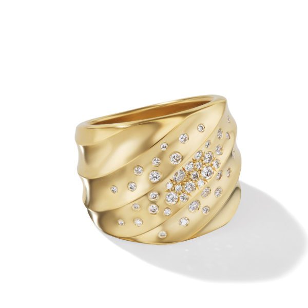 A gold ring with a wavy, textured band design, adorned with numerous small, round diamonds arranged in a scattered pattern, creating a sparkling effect. The ring is set against a plain white background with a soft shadow to the right.