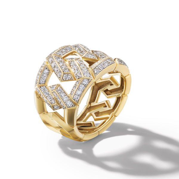 A gold geometric ring with an intricate lattice pattern is adorned with sparkling diamonds. The design casts a complex shadow on a plain white background, highlighting the ring's three-dimensional structure.