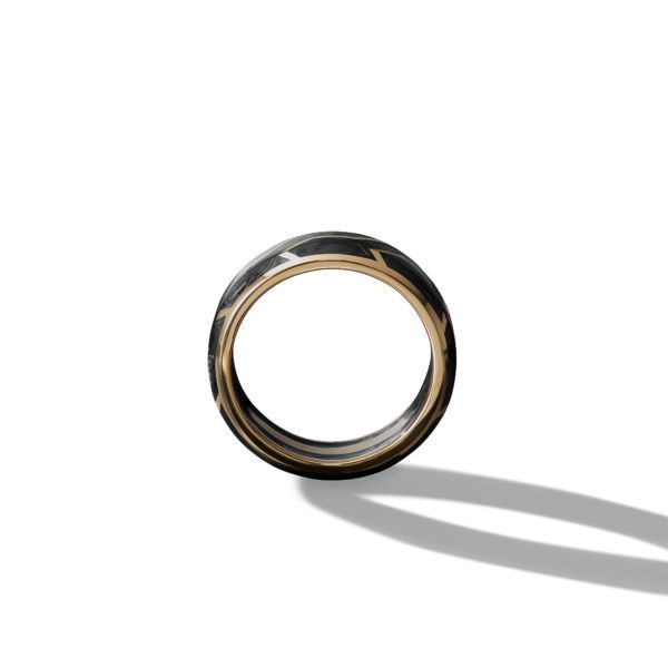 A gold ring with a dark, intricate pattern on the outer surface. The ring is casting a shadow on a white background, emphasizing its round shape and detailed design.