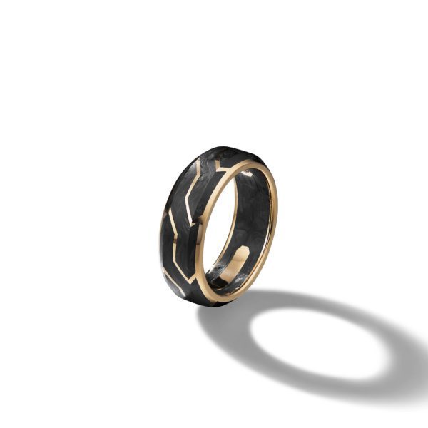 A gold-accented black ring with a geometric design, photographed against a plain white background. The ring casts a shadow to its side, highlighting its polished surface and intricate pattern.