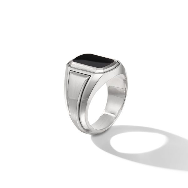 A silver signet ring with a rectangular black stone set in the center is shown against a white background. The ring casts a faint shadow, indicating a light source from the upper left. The design is modern and sleek.