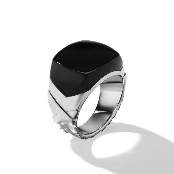 A silver ring featuring a bold, square black gemstone set in a sleek, modern design. The sides of the band have angled grooves, adding a geometric touch to the overall minimalist style. The ring casts a soft shadow on the white surface it rests on.