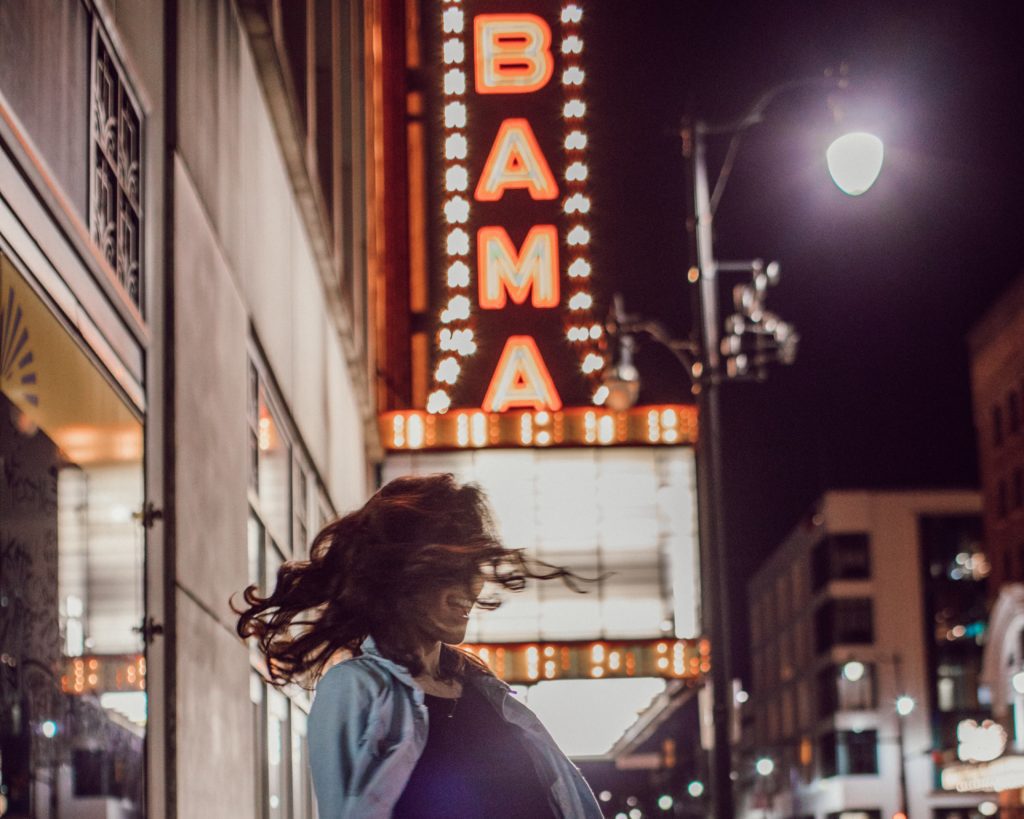 Woman spins beneath the Alabama Theatre sign at night
