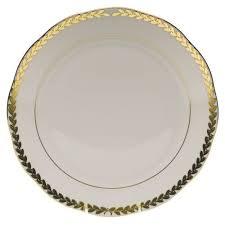 The GOLDEN LAUREL DINNER PLATE is a round white ceramic plate featuring a scalloped edge, beautifully adorned with a decorative golden leaf pattern along the rim.