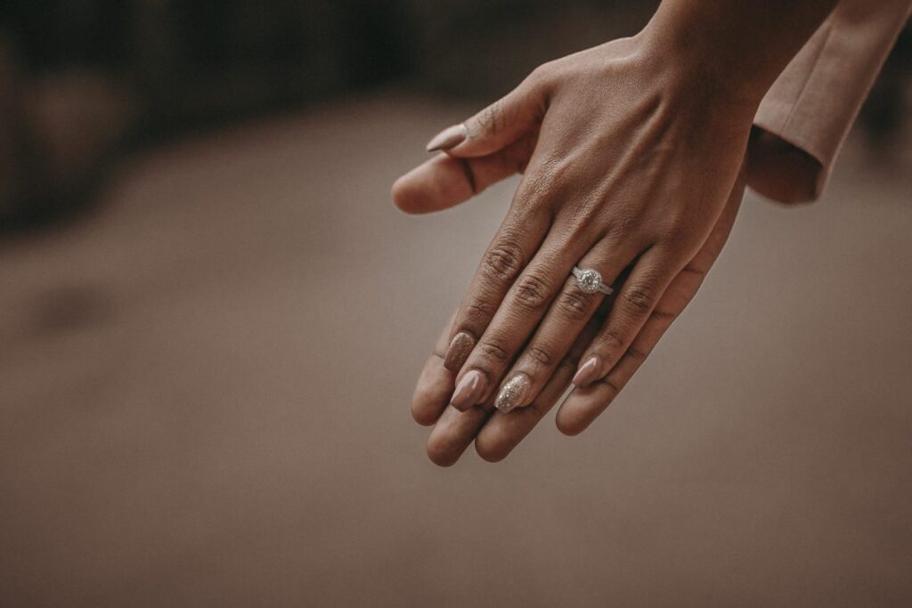 A woman’s hand wearing a white gold and diamond engagement ring, laid over her fiance’s hand