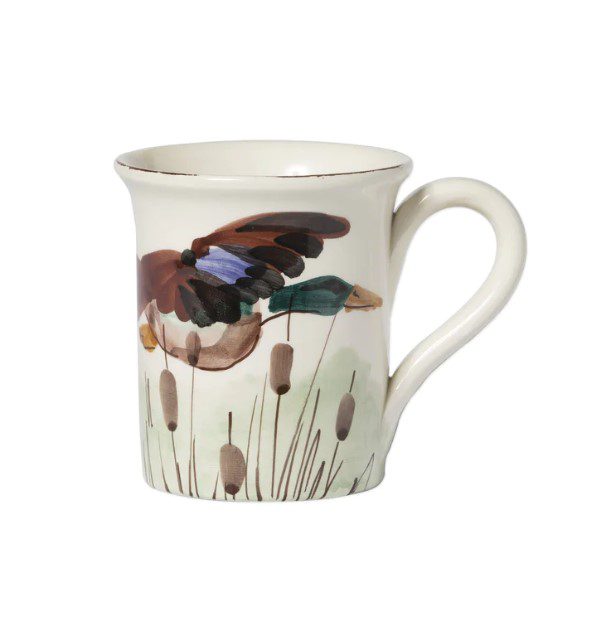 Introducing the Vietri Wildlife Mug - Mallard: a cream-colored ceramic mug with a handle, adorned with a painted design of a duck in mid-flight over brown cattails and green grass along the side. The rim of this exquisite mug features a slightly flared design.