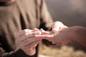 Close-up of a man sliding an engagement ring onto a woman’s hand during a proposal