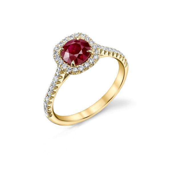 The Bromberg's Signature Collection Ruby and Diamond Halo Ring showcases a striking large round ruby at its center, surrounded by a halo of small white diamonds. The gold band is elegantly adorned with evenly spaced small white diamonds. The image displays the ring against a minimalist plain white background.