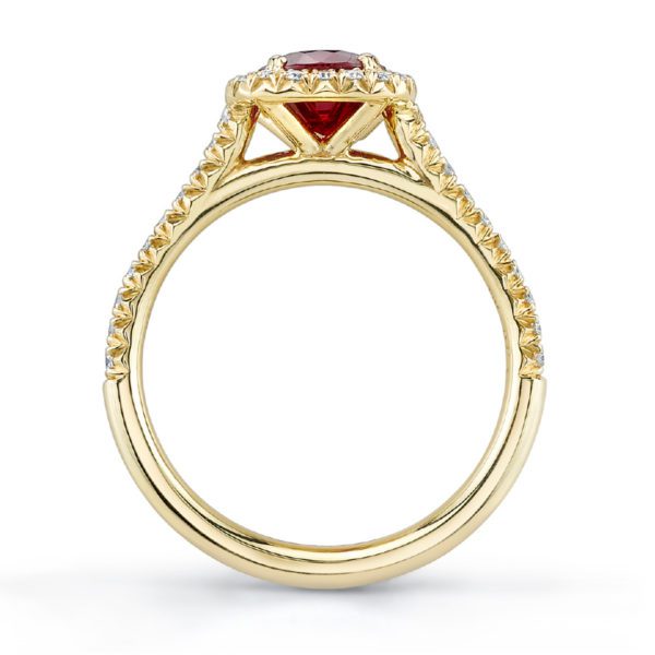 A close-up side view of the Bromberg's Signature Collection Ruby and Diamond Halo Ring showcases its intricate detailing on the band, featuring a round red gemstone as the centerpiece, surrounded by smaller diamond-like stones around the edge. The ring boasts an ornate, elegant design.