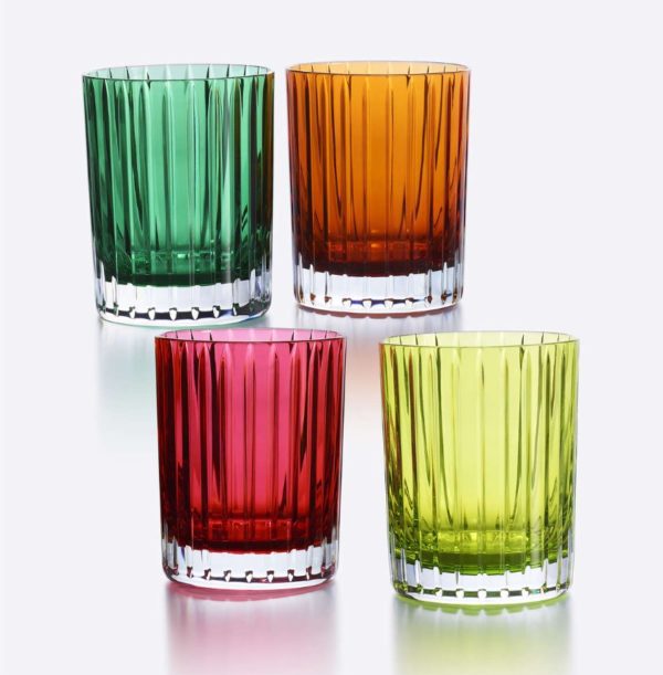 A stunning set of four Baccarat Harmonie Colors of Joy Tumblers is arranged in a square on a reflective surface. Each tumbler is a distinct color: green, orange, red, and yellow. Featuring ribbed textures and clear bases, they create a vibrant and elegant display.