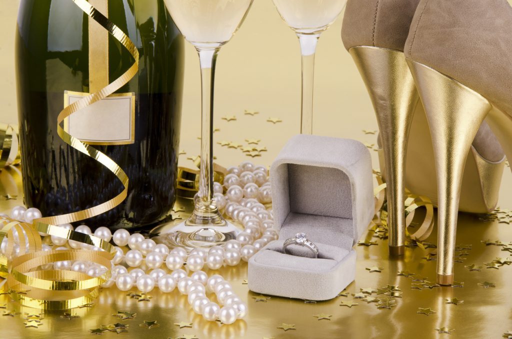 A New Year’s Eve scene with confetti, pearls, a diamond ring, champagne, and high heels
