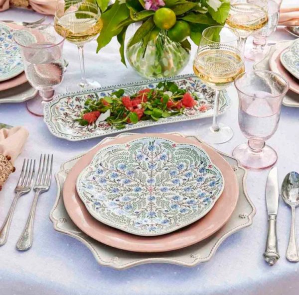 A beautifully set dining table features ornate Juliska Villa Seville Scalloped Salad Plates layered on pastel-colored chargers. The table is adorned with elegant glassware, silver cutlery, and a floral centerpiece. A rectangular platter with a salad sits in the middle.