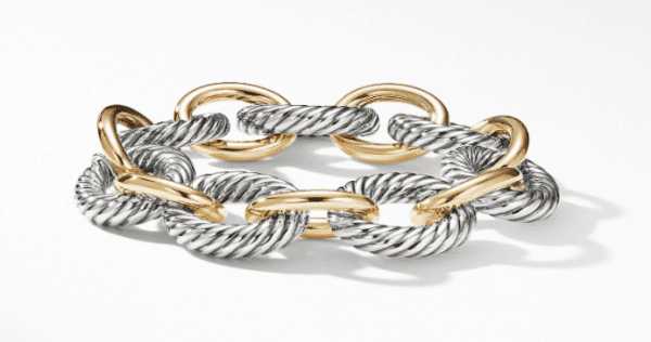 The XL OVAL LINK BRACELET features a stunning design with alternating silver and gold oval links. The silver links showcase a twisted, rope-like texture, while the gold links are smooth and shiny. Displayed in a circular arrangement against a plain white background, this bracelet exudes elegance.