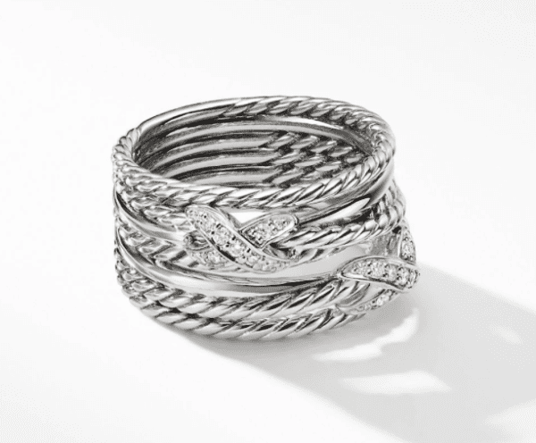 Presenting the PAVE CROSSOVER 2 "X" RING, a masterfully designed silver ring showcasing interwoven twisted rope-like bands. Select sections of the ring are embellished with tiny, shimmering diamonds, contributing to its sophisticated and intricate appearance. The ring casts a delicate shadow on the white surface it rests upon.