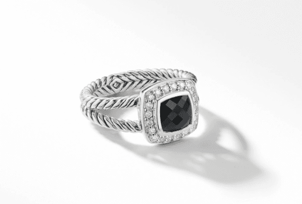 The 7MM PETITE ALBION RING is a sophisticated piece featuring a black, square-cut gemstone encircled by a halo of small, clear stones. The band boasts a braided rope design, enhancing its elegant appearance. The ring casts a soft shadow on the white background.