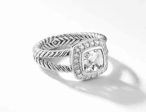 A 7MM PETITE ALBION RING featuring a twisted band design and an impressive large, square-cut clear gemstone at its centerpiece, encircled by a halo of smaller, round clear stones. The ring casts a soft shadow on the white surface beneath it.