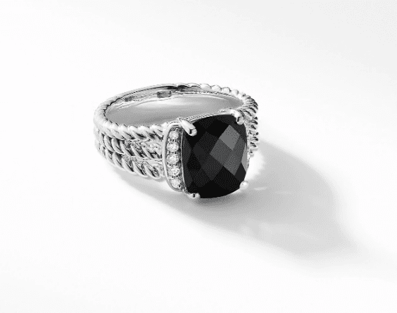 The PETITE WHEATON RING BO is a silver ring with a distinctive large, black, oval-shaped gemstone at its center, accompanied by small, round, white stones on each side and set on a band with an intricate rope-like design.