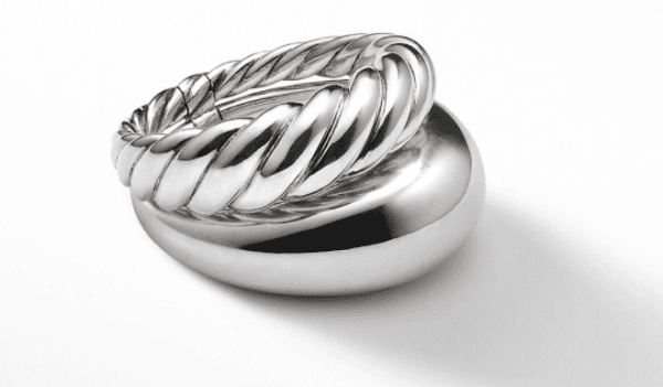 The PURE FORM 2 ROW RING, with its shiny silver and twisted rope-like design complete with a clasp, rests elegantly atop a smooth, solid, and rounded silver base. The reflective base with its flat bottom creates a simple yet elegant display against a white background.