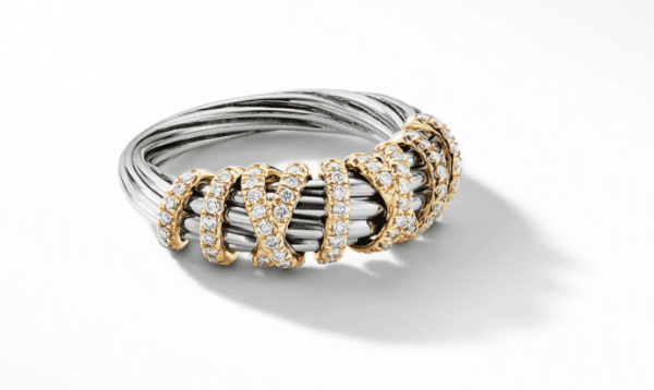 The 8MM HELENA NARROW RING showcases a silver-toned structure with multiple intertwined bands, elegantly adorned with sparkling diamonds set in gold. The ring casts a shadow on the white background, highlighting its intricate design and the gleaming contrast between the metals and gemstones.