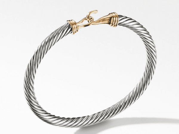 The 5MM BUCKLE BRACELET is a twisted cable bangle featuring a mix of silver and gold tones. It boasts a rope-like design with a sleek, polished finish, complemented by a gold hook clasp at the top. Set against a plain white backdrop, the bracelet's elegant and minimalistic design is accentuated beautifully.