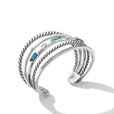 The STAX NARROW BRACELET IB BT DI is a silver cuff bracelet showcasing a twisted rope-like design. It features three distinct rows, each embellished with rectangular blue gemstones and small clear crystals arranged in a linear pattern. This elegant piece casts a soft shadow on a white background.