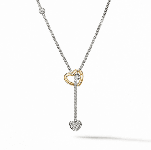 Introducing the CABLE HEART Y NECKLACE: a delicate piece that features a two-tone heart design. This elegant necklace has a silver chain adorned with an intertwined gold and silver heart pendant at the center, complete with a dangling silver heart charm. A small gemstone nestled between the hearts adds a touch of sparkle to this exquisite accessory.