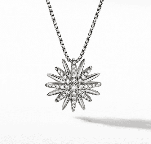 A close-up image of the 19MM STARBURST PENDANT, a silver necklace with a starburst pendant. The pendant has numerous points and is encrusted with small diamonds, giving it a sparkling appearance. The chain appears to be made of small interlocking links. The background is white.