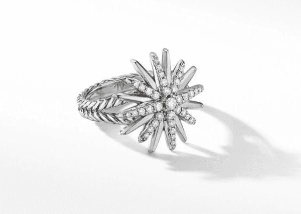 A close-up of the 19MM STARBURST RING, showcasing a sunburst design embellished with small, sparkling white stones. The band features a textured twisted rope pattern, and the image casts a light shadow on a white background.